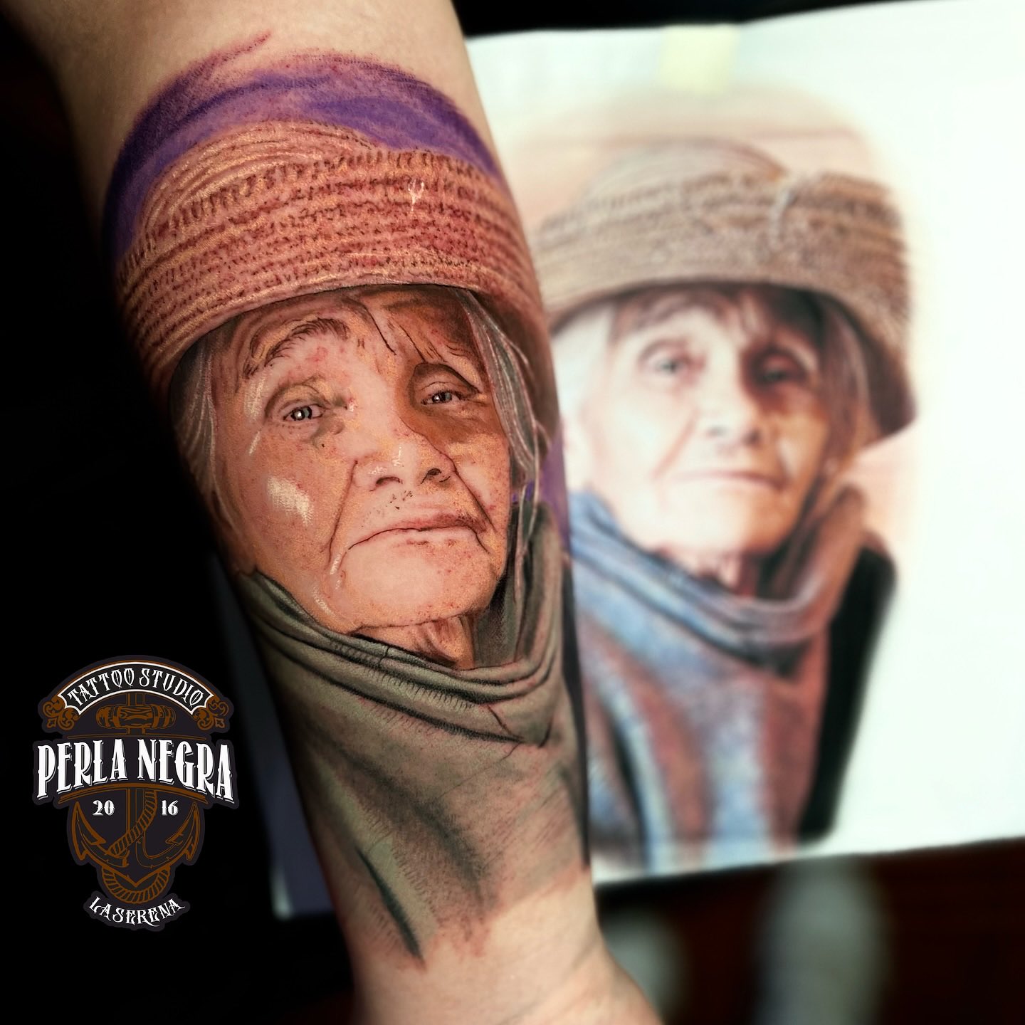 El retrato tatuado de una señora mayor en un antebrazo, junto a la fotografía impresa desde la que se hizo.