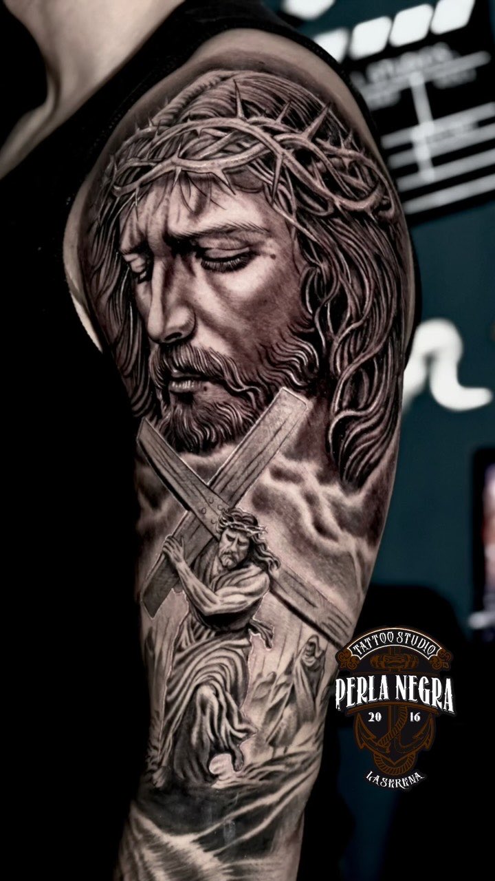 Cristo con la corona de espinas, en negro y gris, tatuado en un brazo.