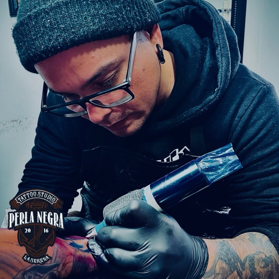 Rodrigo tatuando: gorro de lana, guantes negros y la máquina envuelta en film azul.