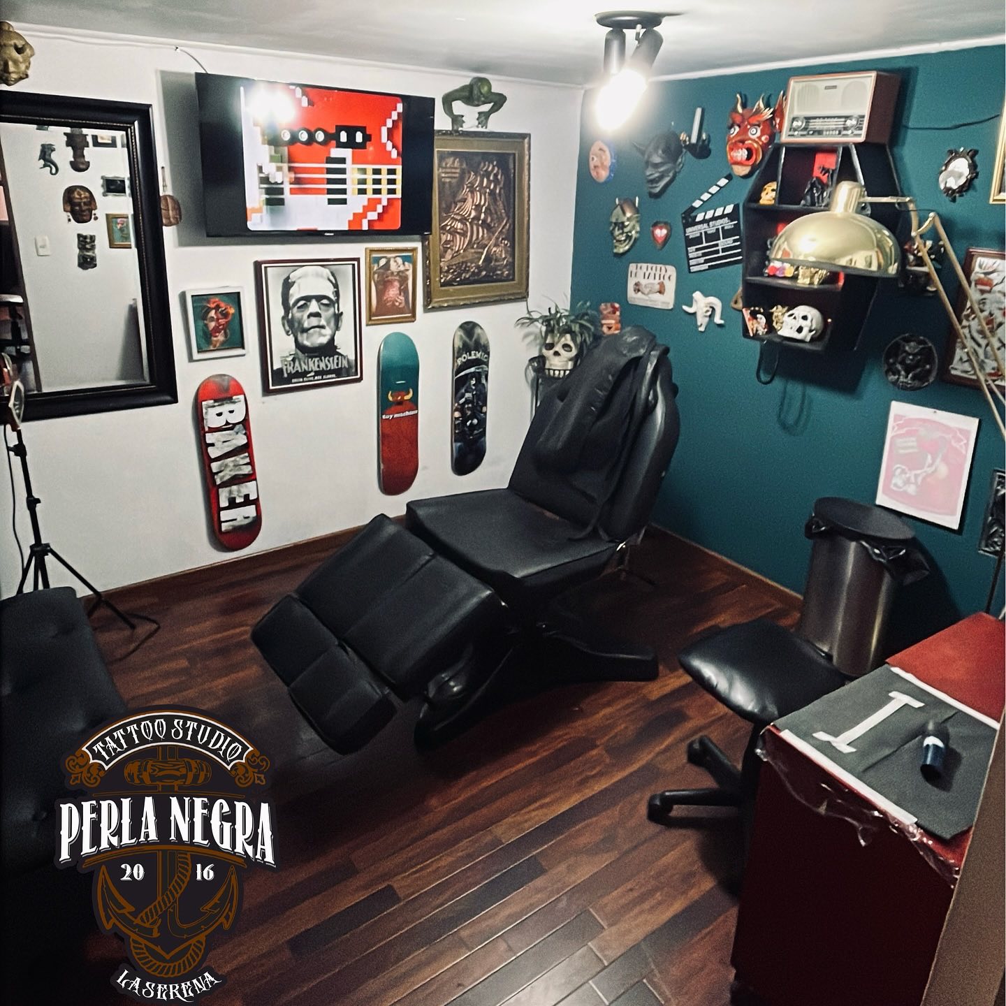 Interior del studio: pared azul petróleo con cuadros y máscaras, camilla negra y piso de madera.