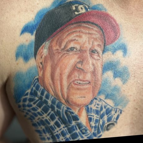Retrato cicatrizado de un hombre mayor con gorra, tatuado en la espalda.