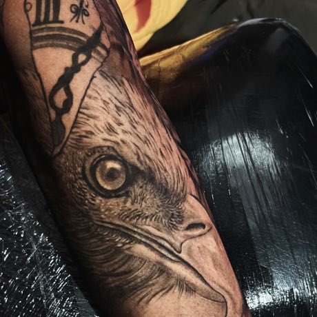 Cabeza de ave y un reloj en negro y gris, cicatrizados en un antebrazo.