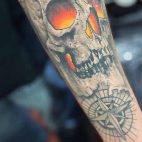 Calavera con los ojos encendidos y una rosa de los vientos, cicatrizada en un antebrazo.